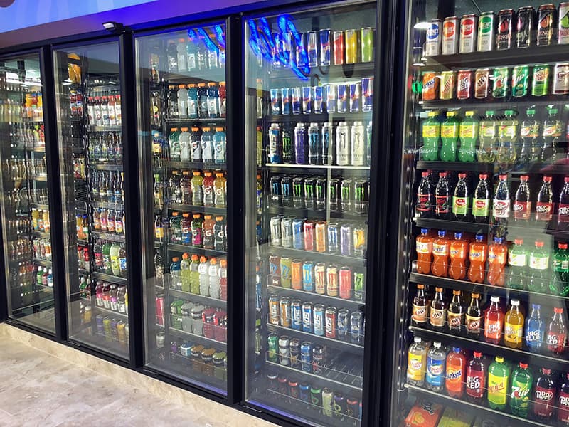 Glass-door convenience-store cooler stocked with drinks on FlexRoller shelves